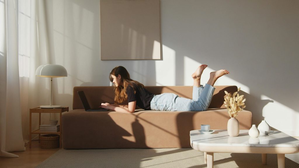 Mujer relajada en un sofá, trabajando con el ordenador en un interior minimalista.